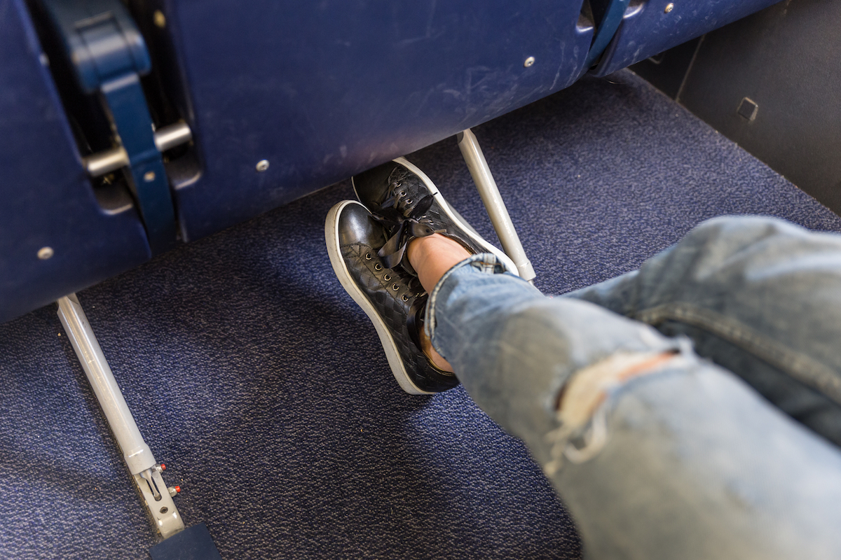Female sitting in an airplane seat stretching her legs, wearing ripped jeans and black sneakers