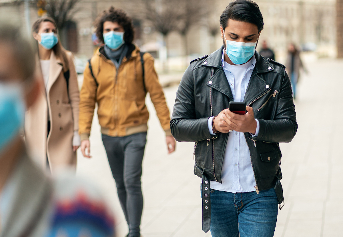 Portrait of young man on the street wearing face protective mask to prevent Coronavirus using smartphone