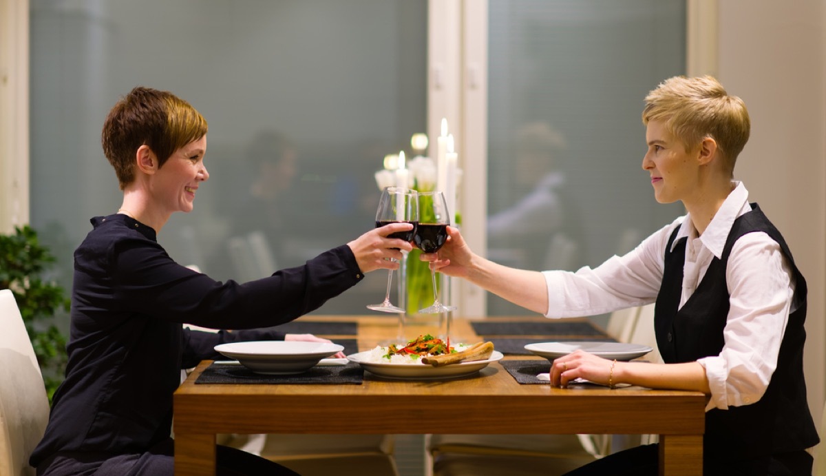 two white women toasting red wine over meal at home