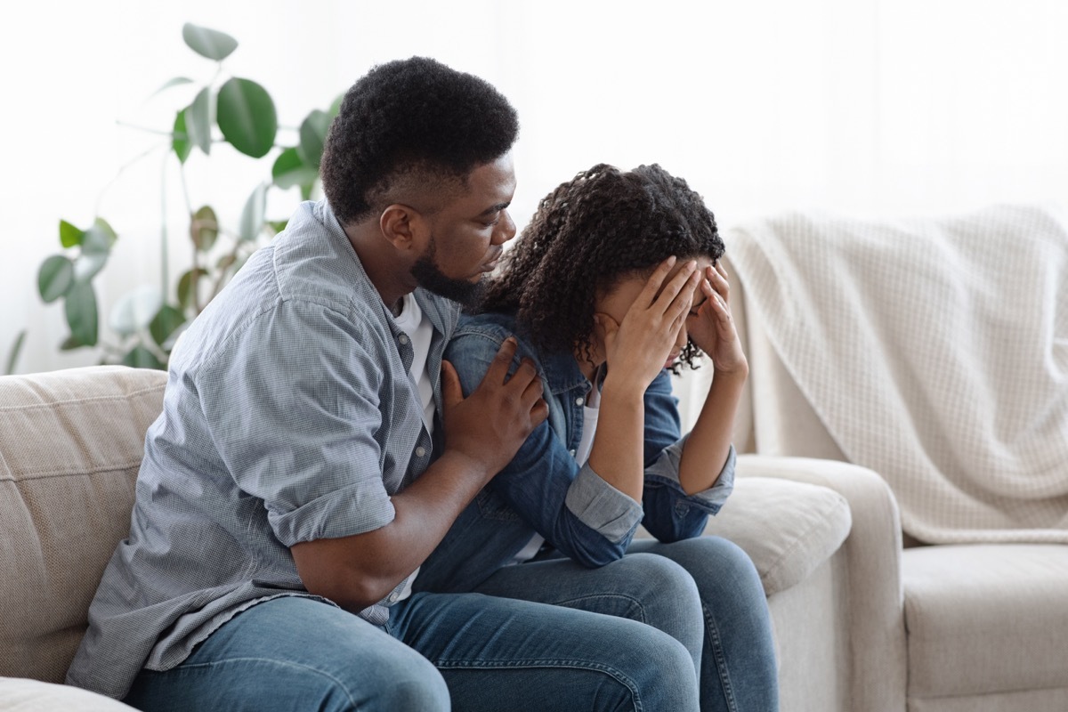 Dependent Relationship Concept. Young Guy Soothing His Depressed Girlfriend At Home, Embracing Her On Couch In Living Room