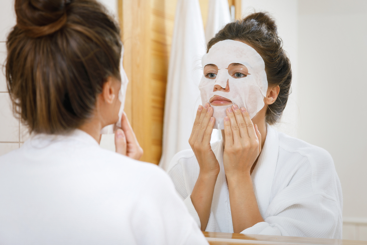 Woman is applying sheet mask on her face in the bathroom