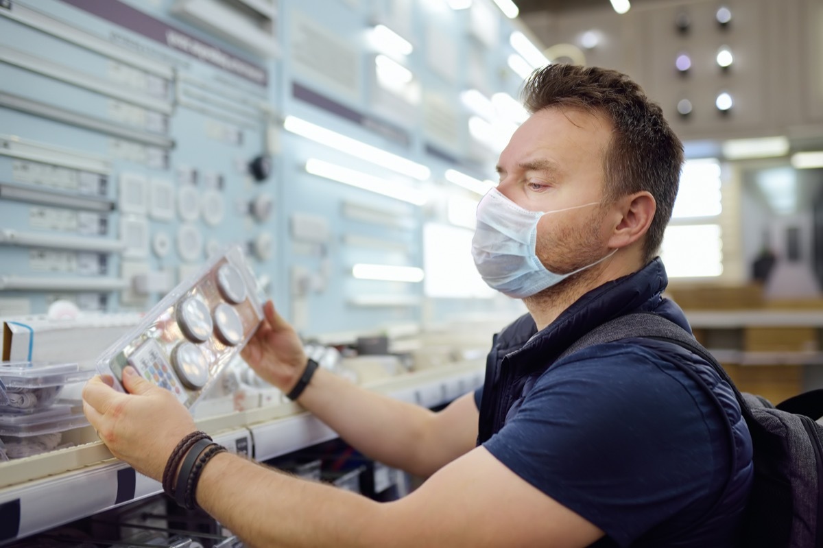 Middle age man wearing protection facemask choosing electric lamps in a hardware store.