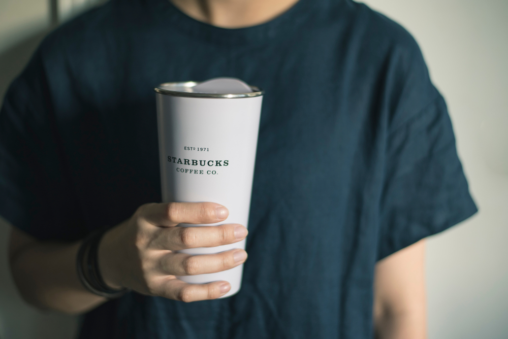 A person holding a reusable Starbucks thermal cup