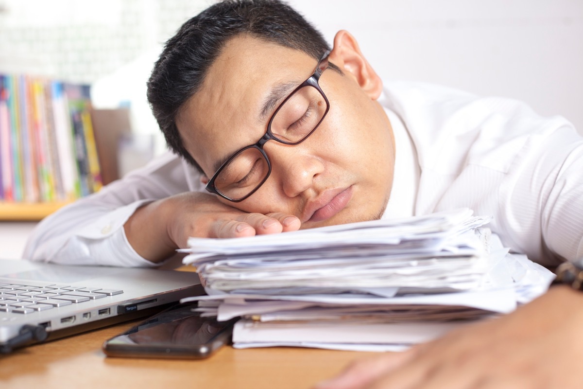 man napping on a stack of papers at his desk