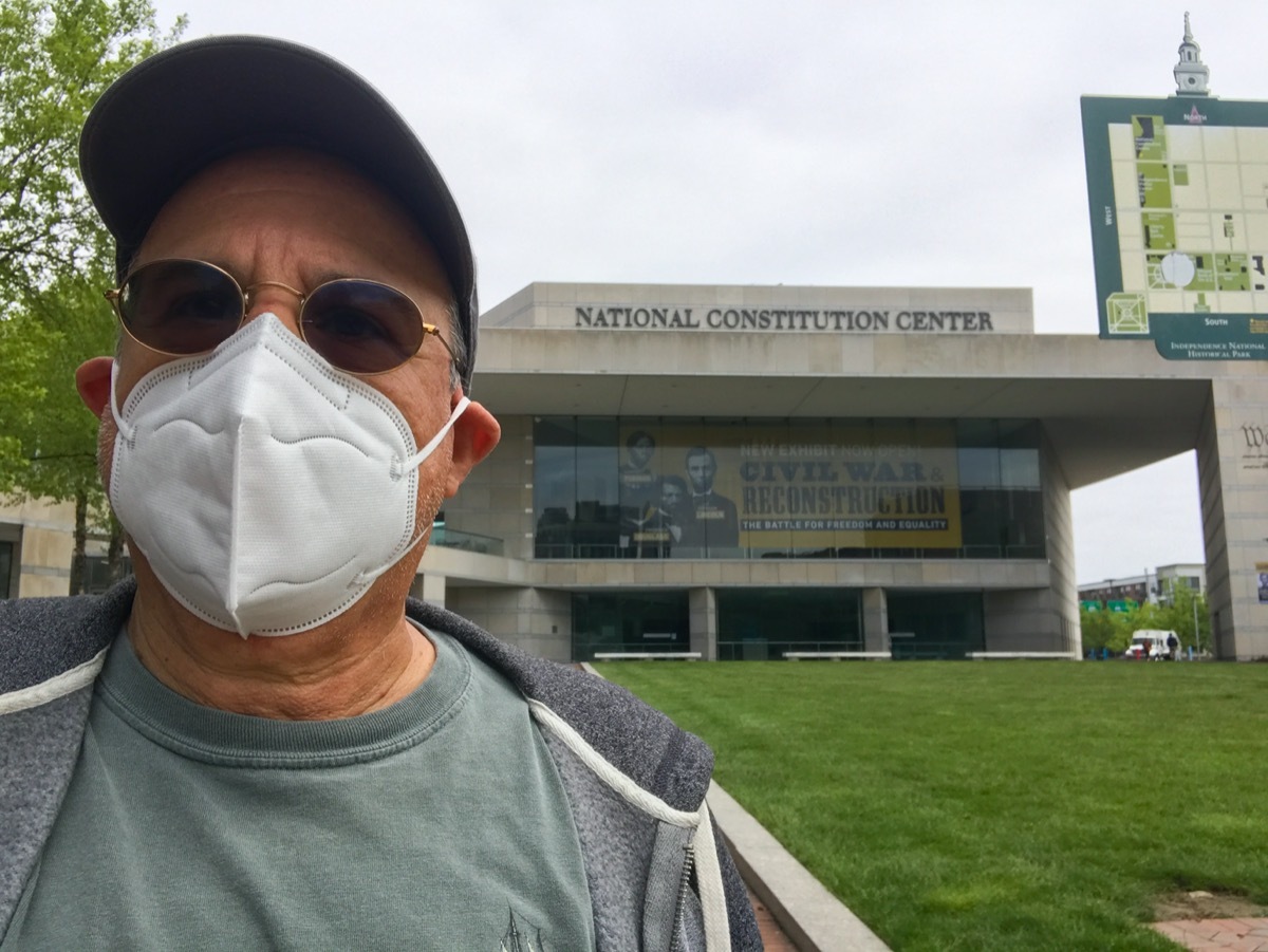 Older man wearing a KN 95 mask on his face stands in front of the National Constitution Center in Philadelphia
