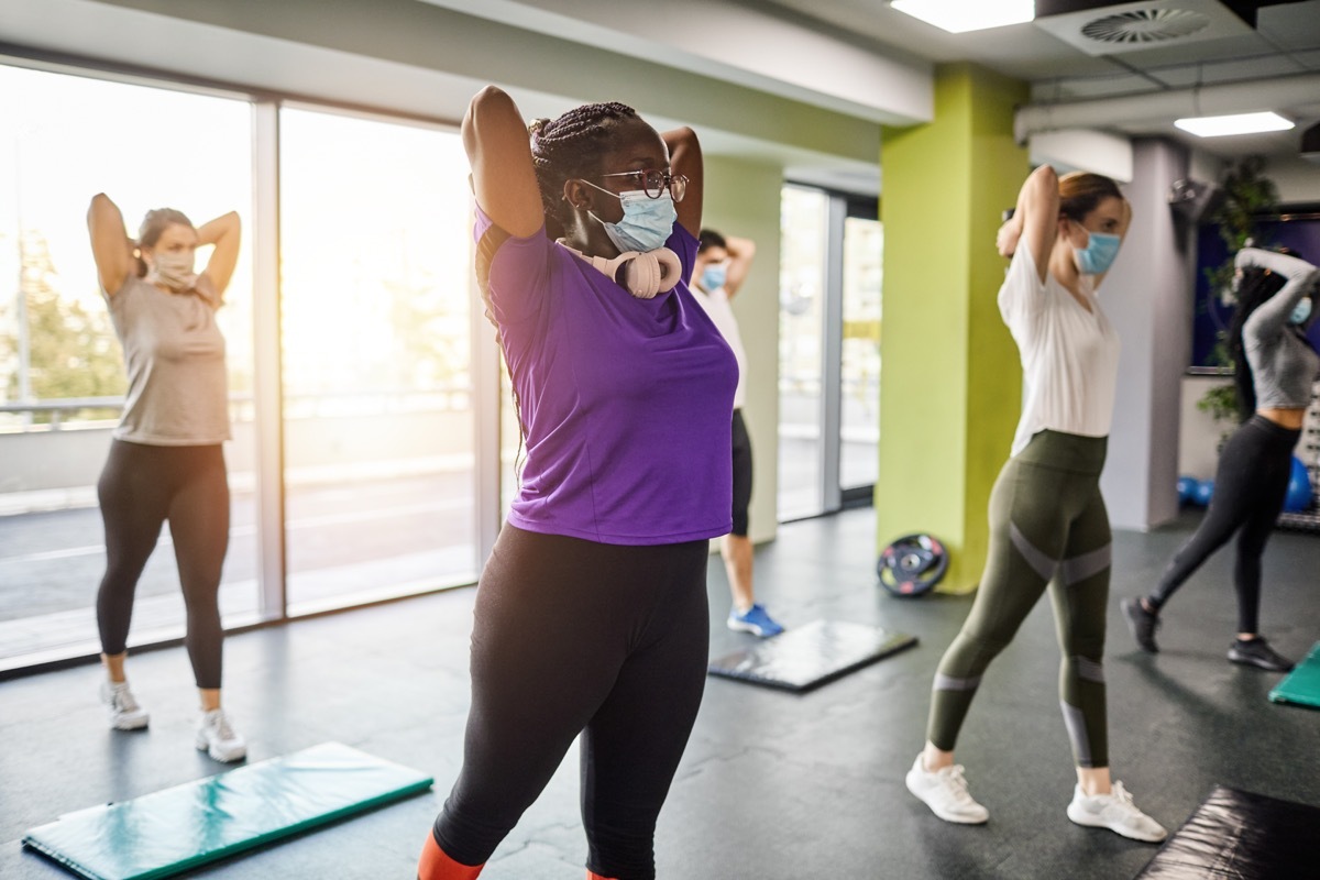 Group of women exercising with protective face masks in the gym after coronavirus pandemic. Reopening business concept.