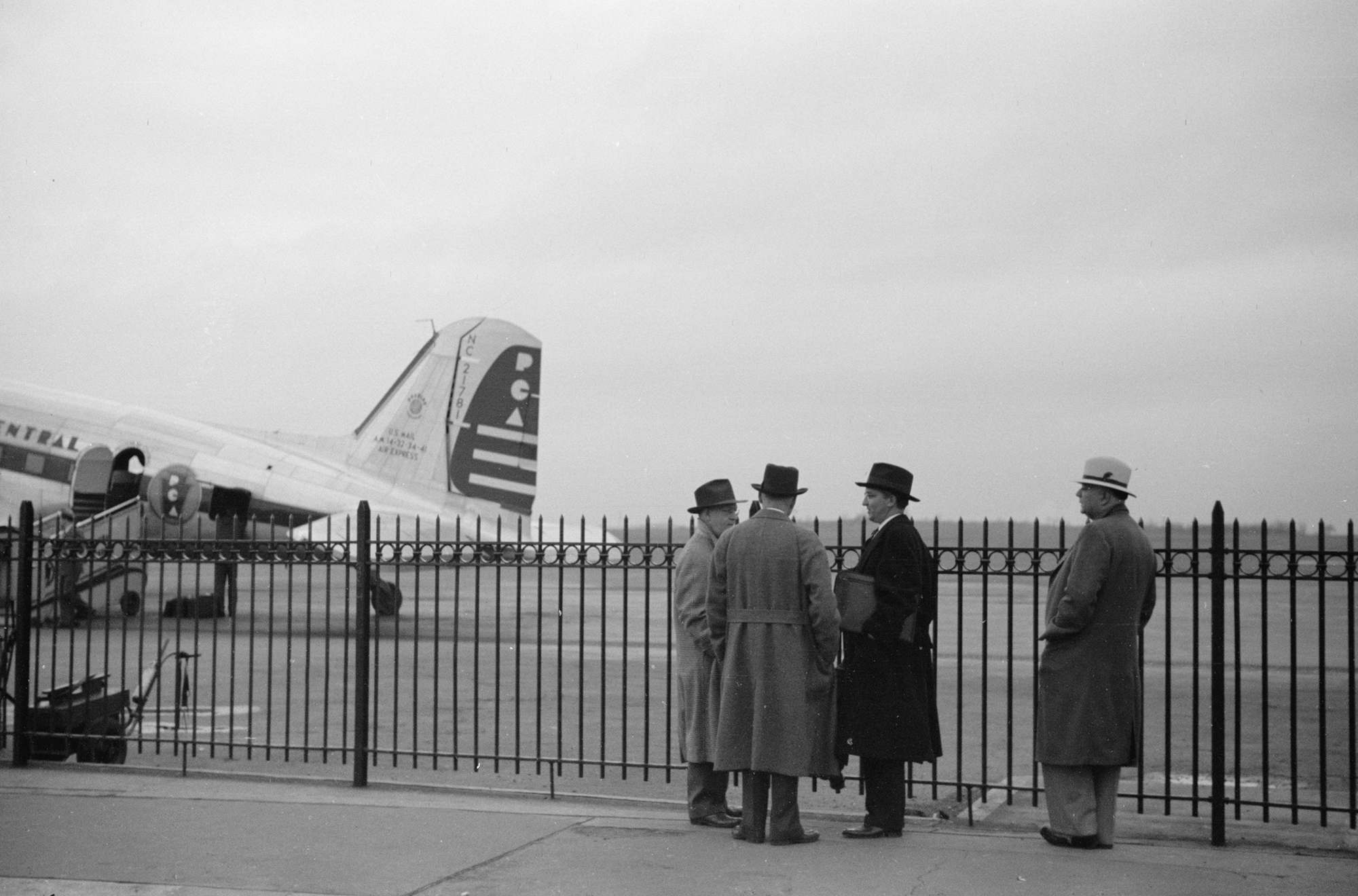 four men wait for a plane to land on the tarmac