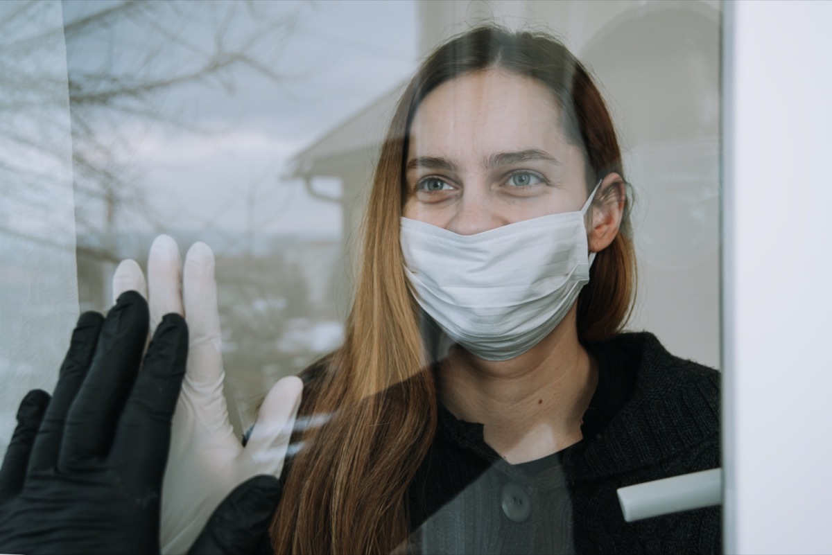 happy woman seeing her fried who came to visit her due to coronavirus covid-19 wit mask and gloves on window at home