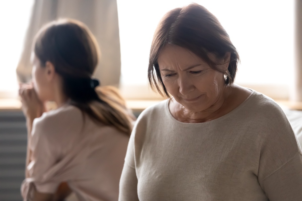 Head shot offended middle aged desperate woman sitting separately on couch with ignoring grownup daughter on background. Frustrated unhappy senior mature mother feeling despair after quarrel.