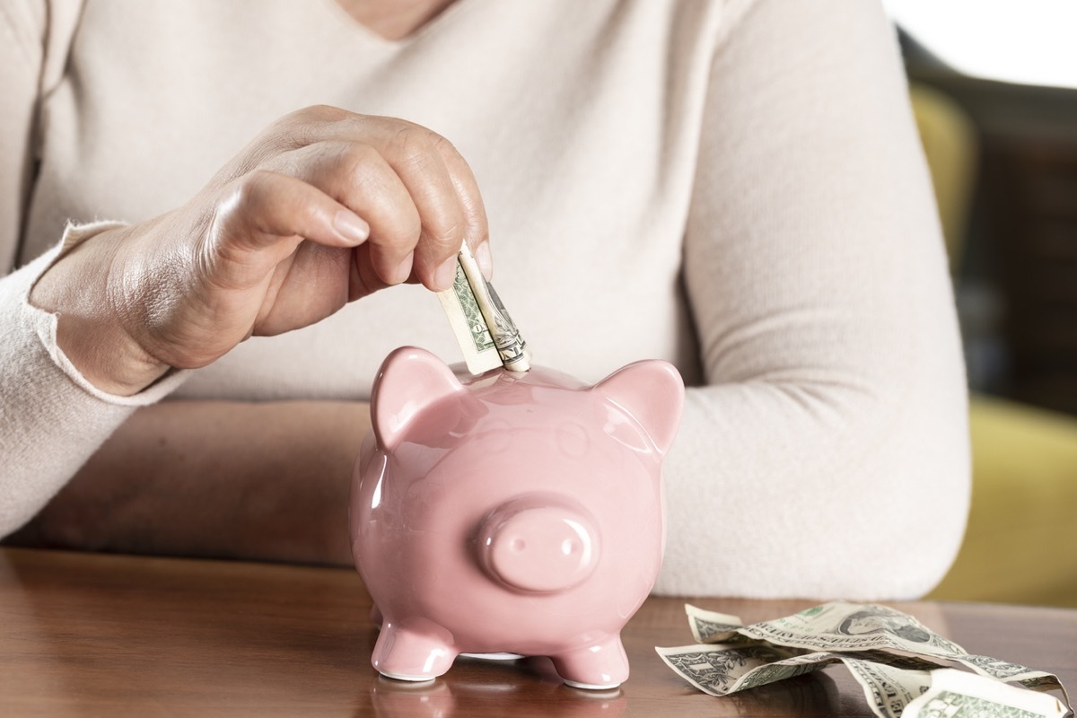 close up of woman putting money in a pink piggy bank