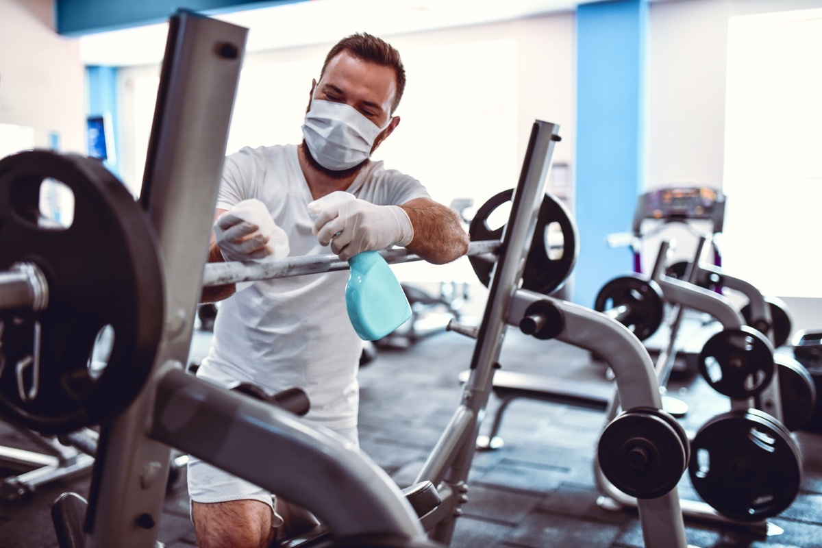 Gym Worker Disinfecting Barbell Rack To Prevent Coronavirus Spread
