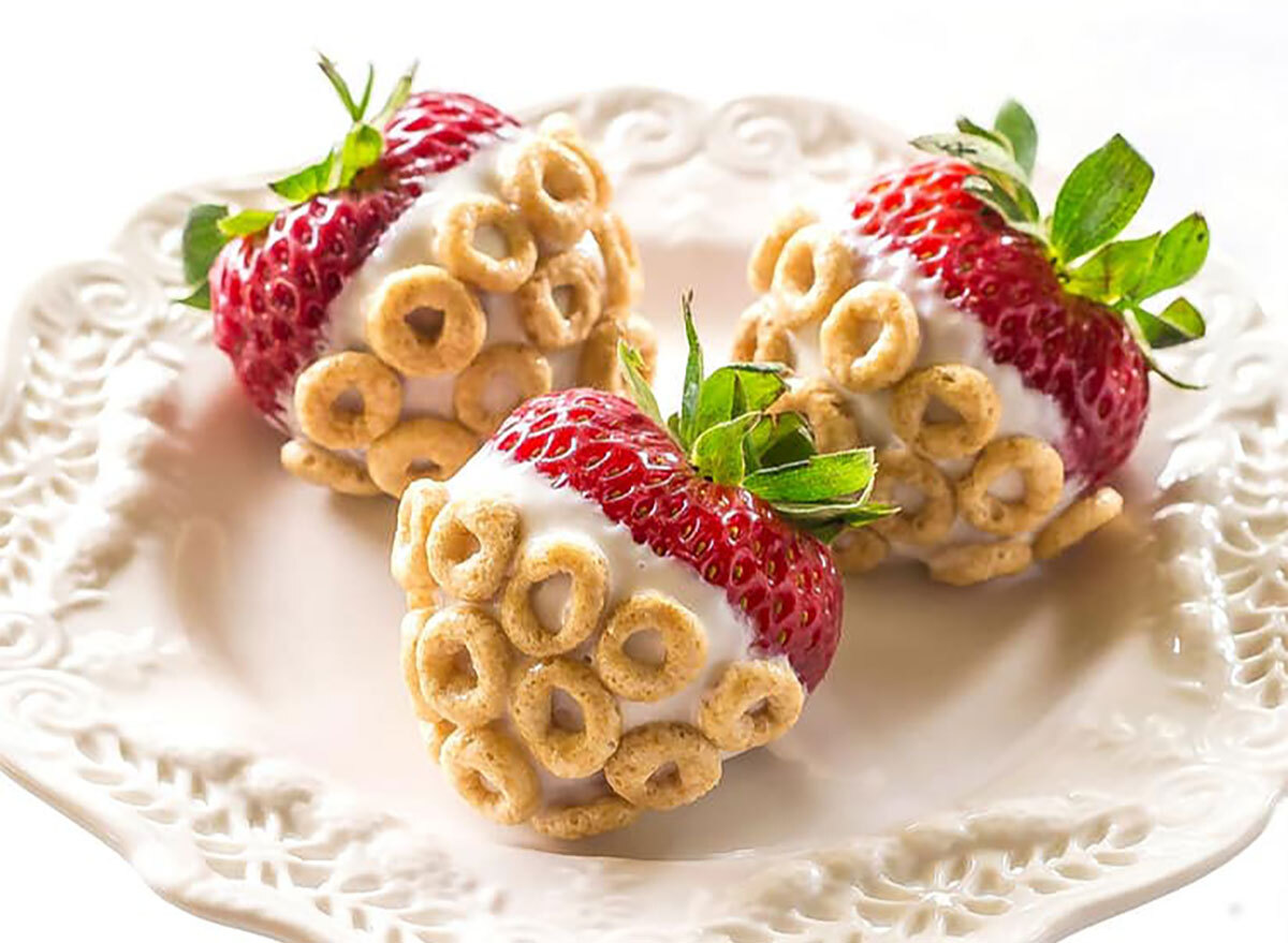 whole strawberries dipped in yogurt and covered with cheerios on white serving plate