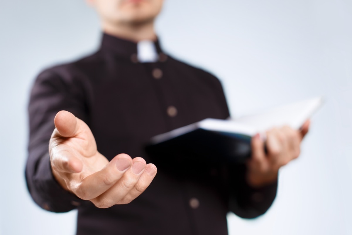 Priest with his hand out and holding a bible