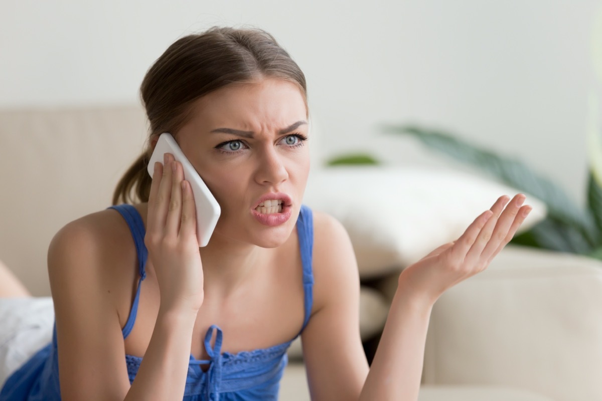 Angry young woman arguing talking on phone at home