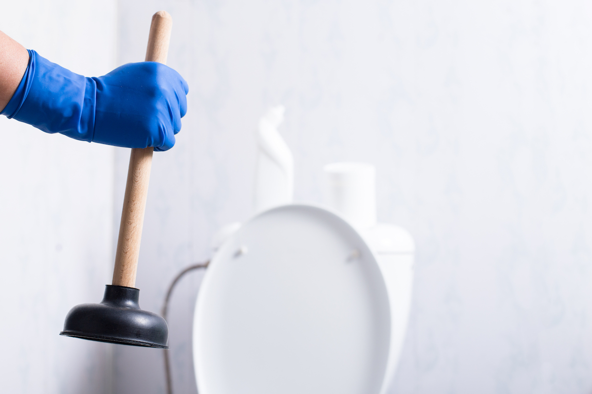 hand in blue glove with toilet plunger over toilet
