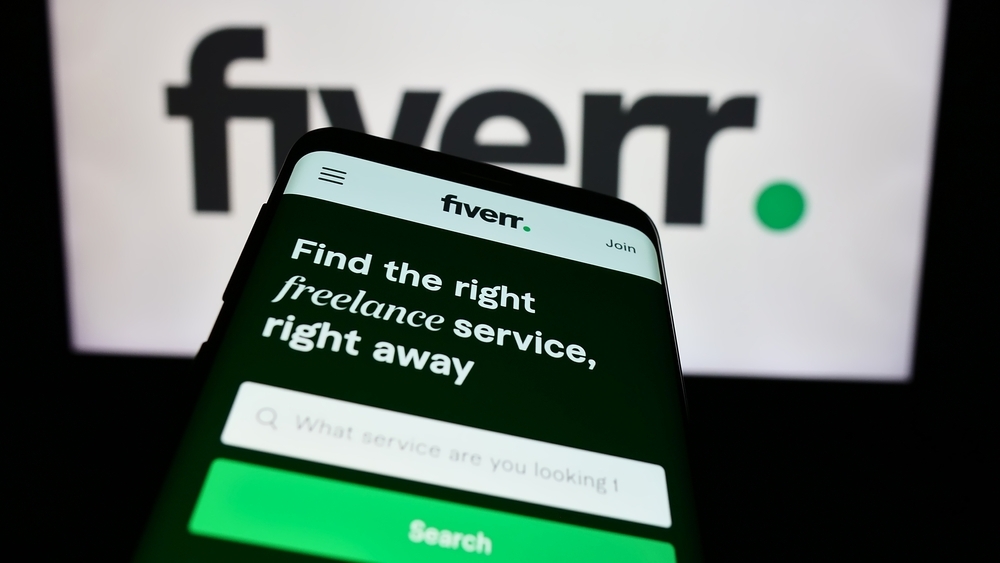 A close up of the Fiverr website on a phone screen in front of a computer screen.