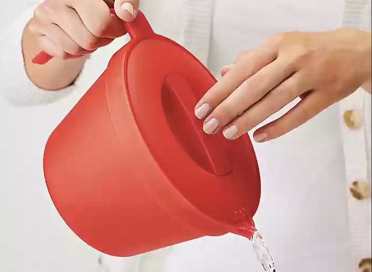 woman's hand pouring water from red kettle