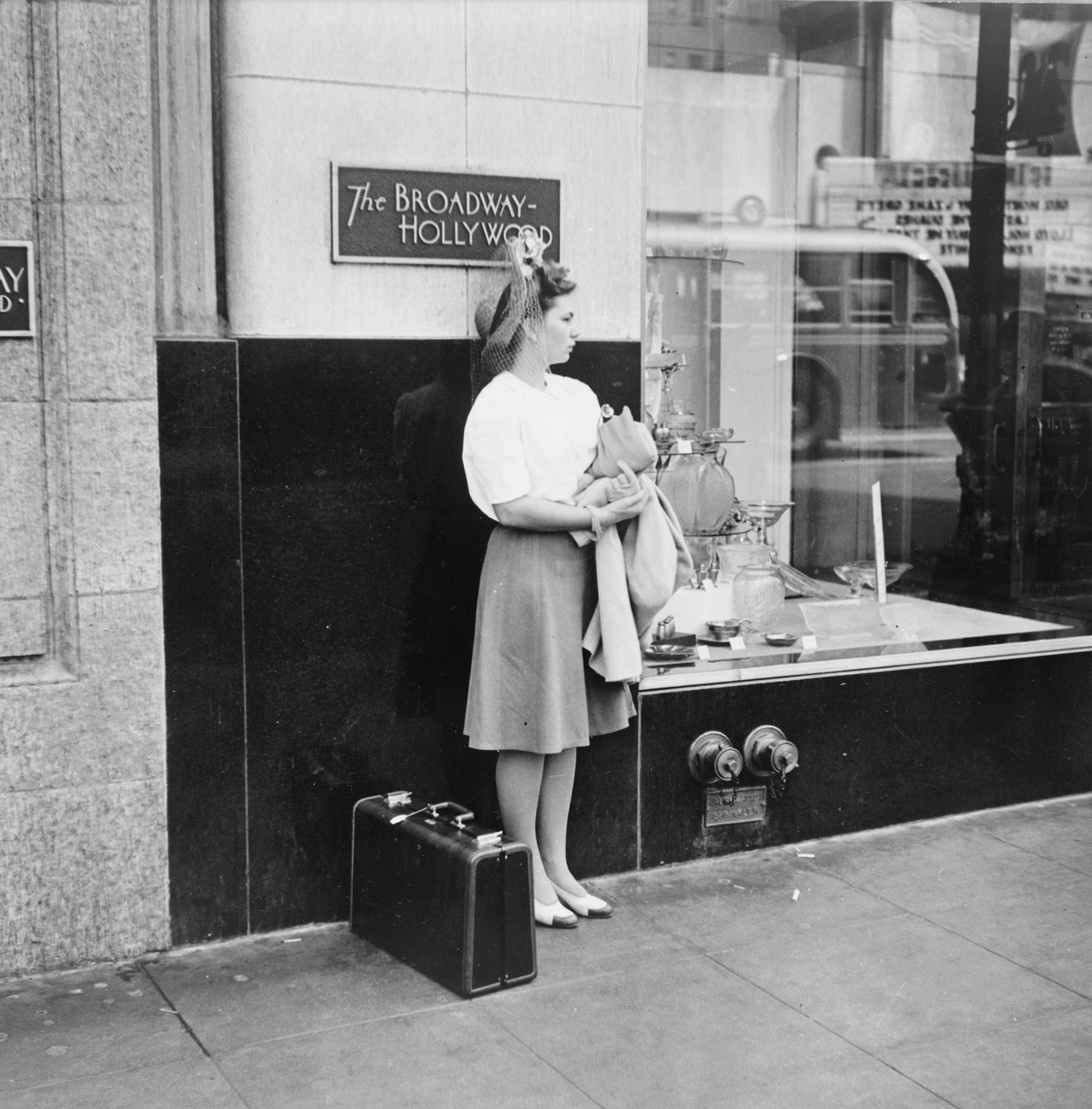 a young woman waits on hollywood boulevard with her suitcase