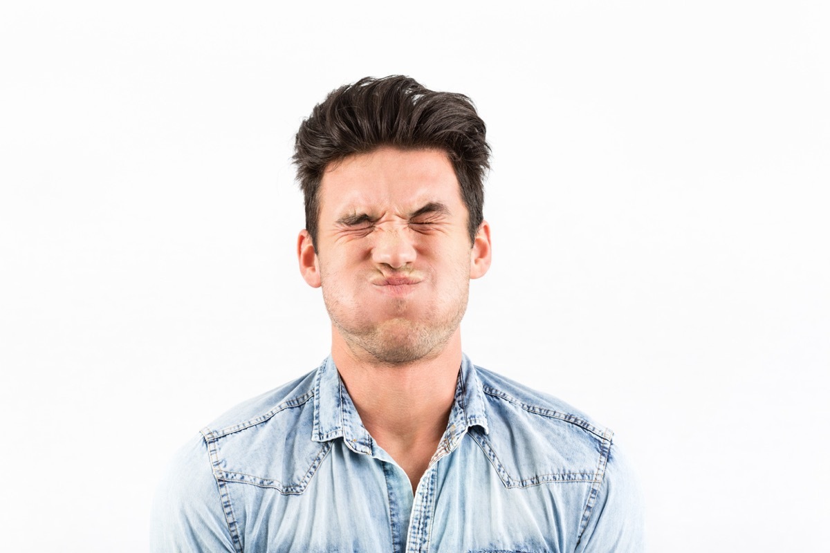 Young white man making a face while holding his breath amid white background