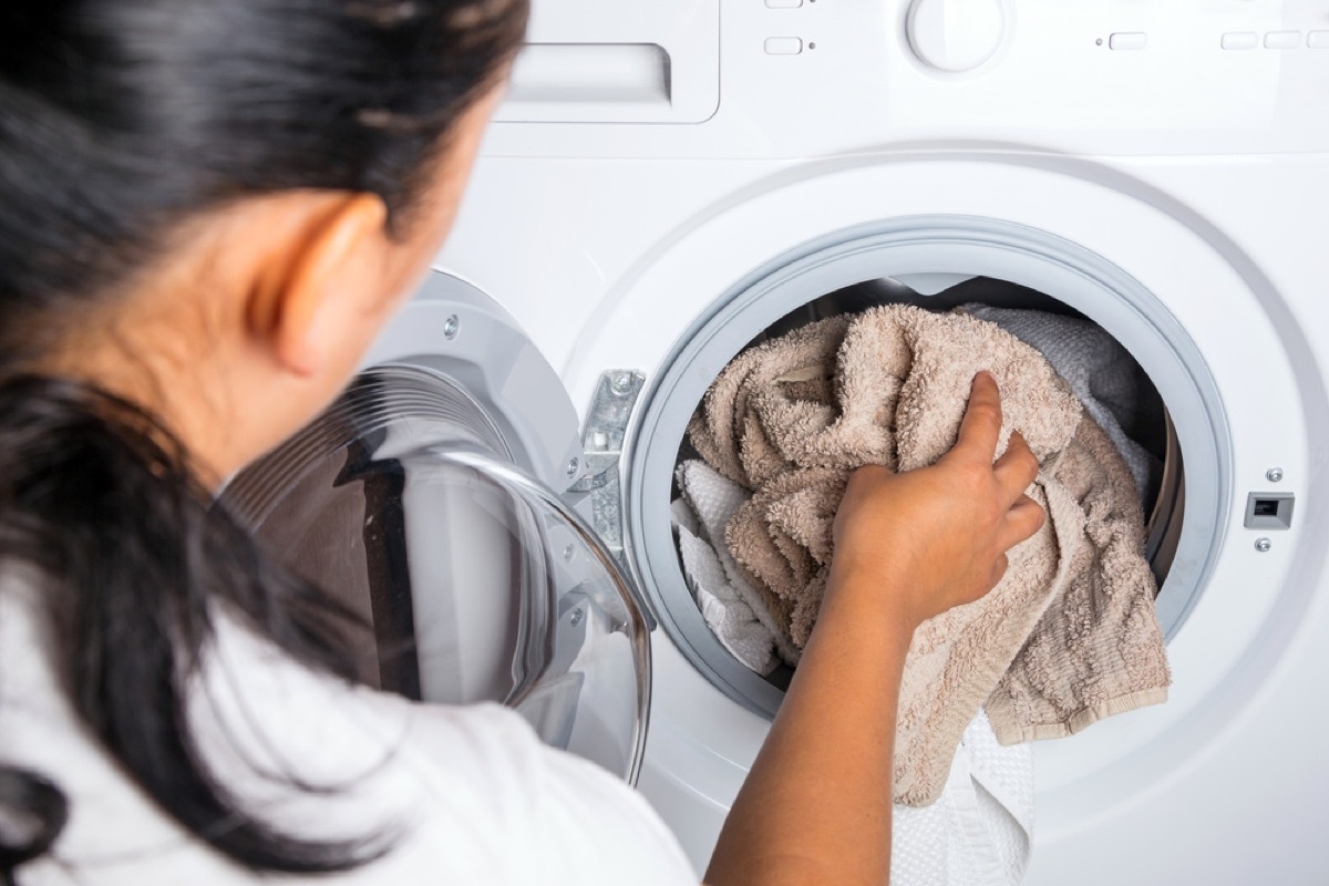 woman putting towel in washing machine, old school cleaning tips