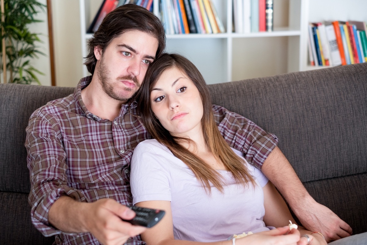young white couple watching tv together and looking bored