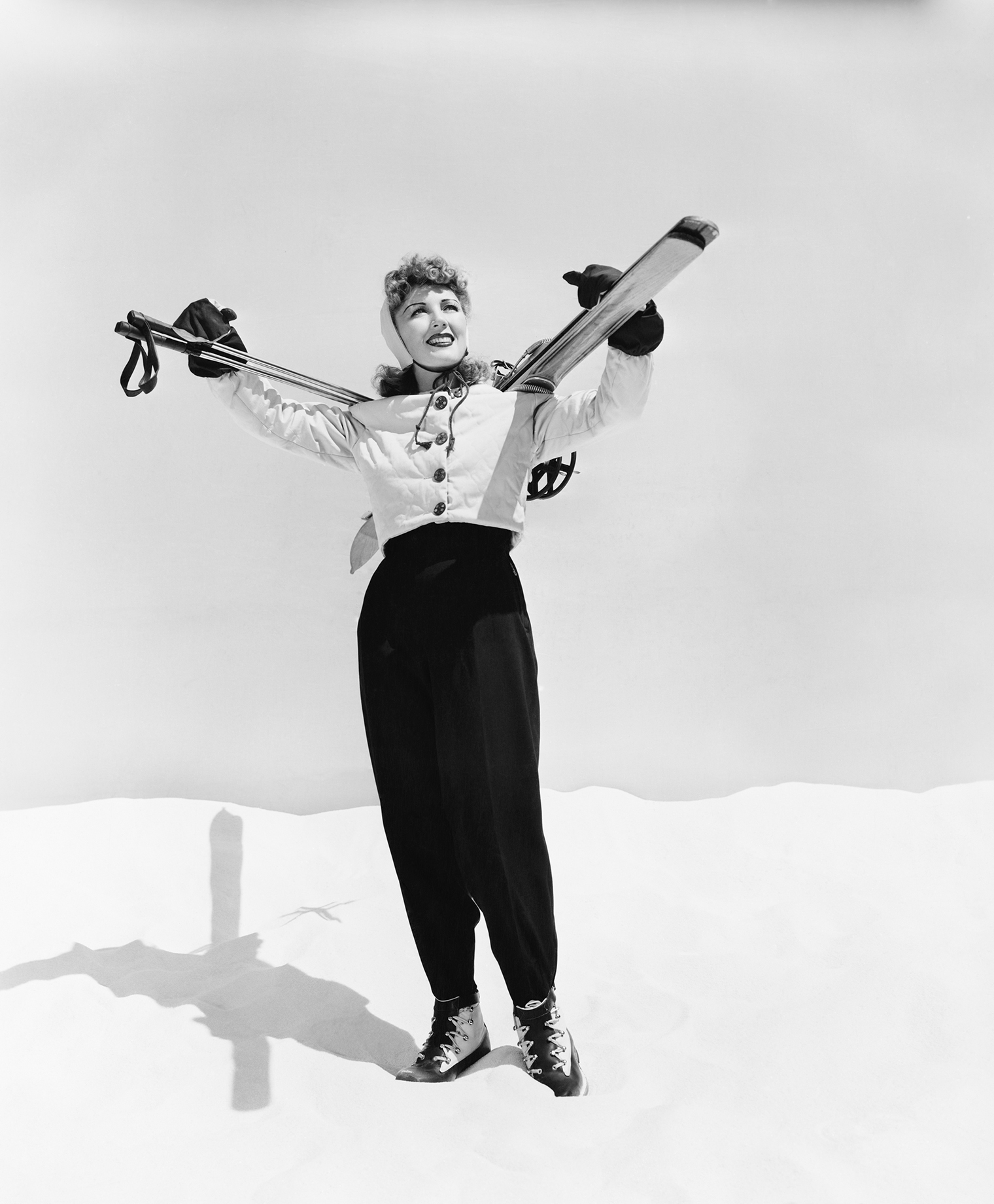 a female skier poses in snow with her skis on her shoulders