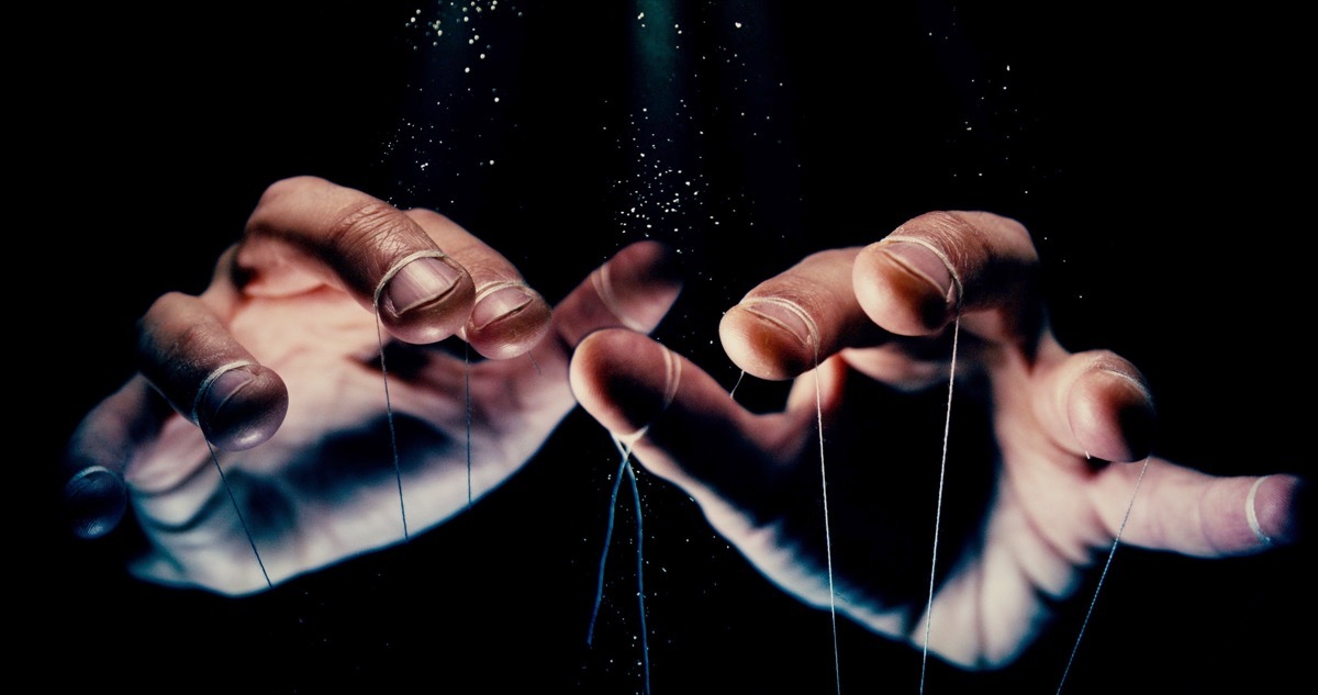 control concept photo with black background shows hands with strings tied to them, like a puppet master