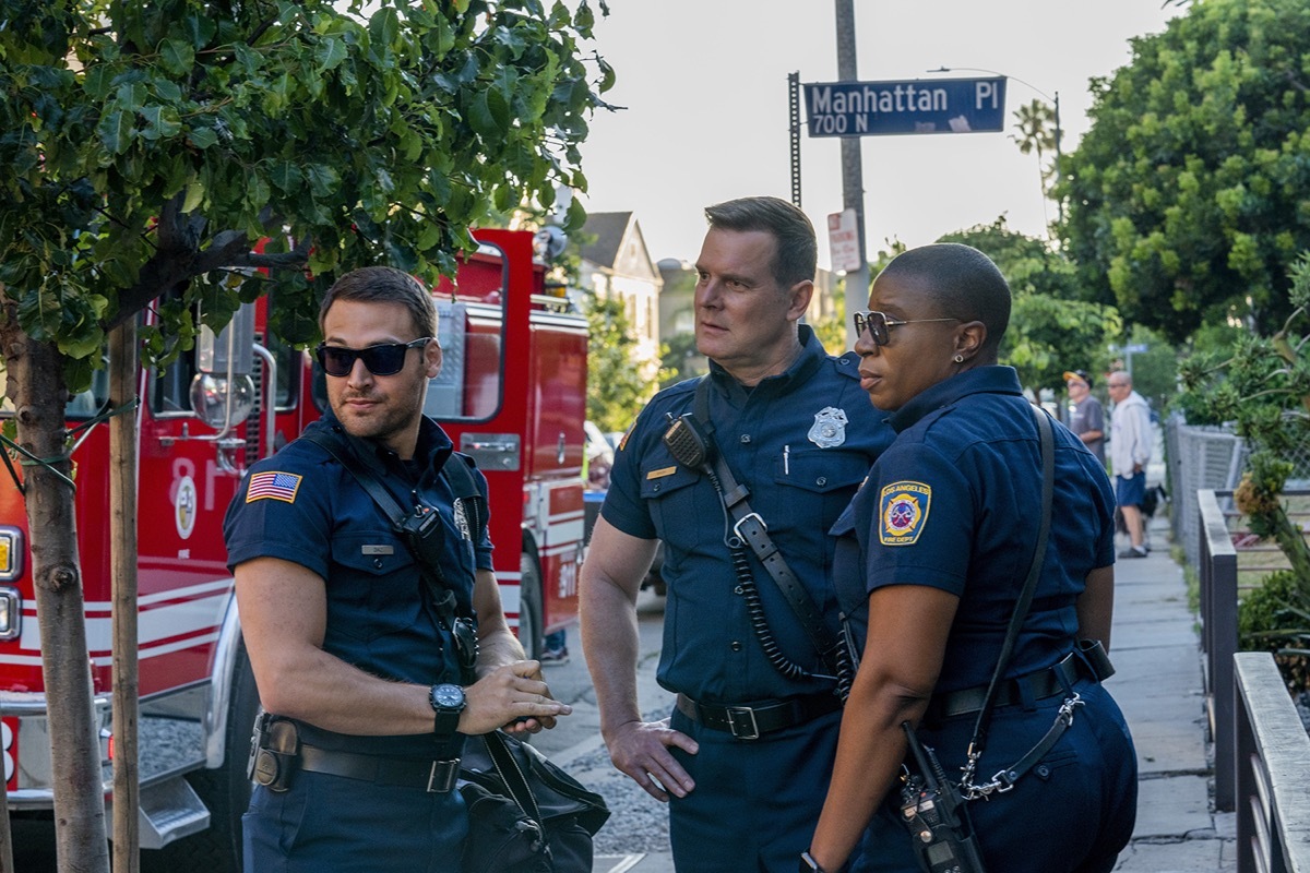 the cast of 9-1-1 standing on a street in front of a firetruck