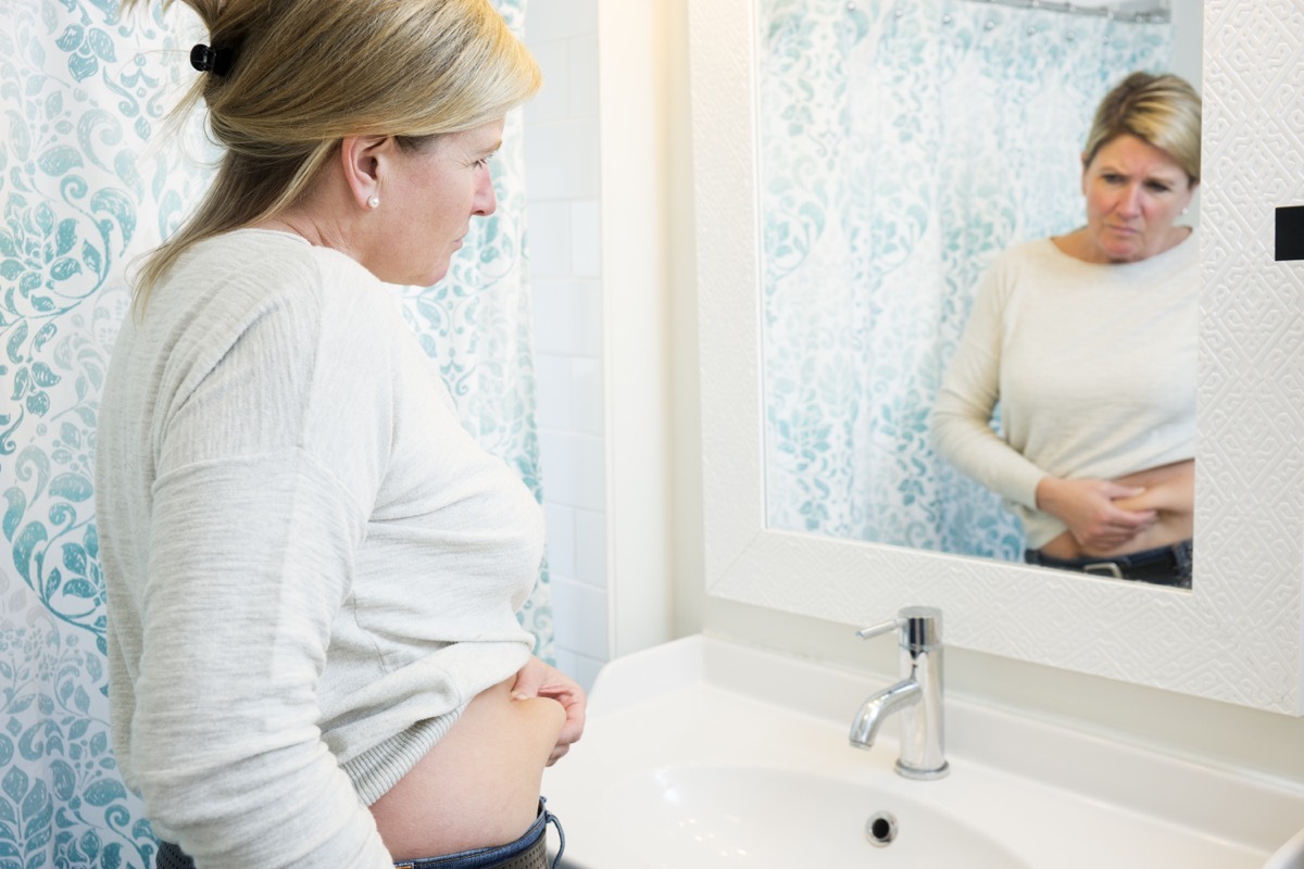 Woman pinching her stomach and looking in the mirror because she gained weight