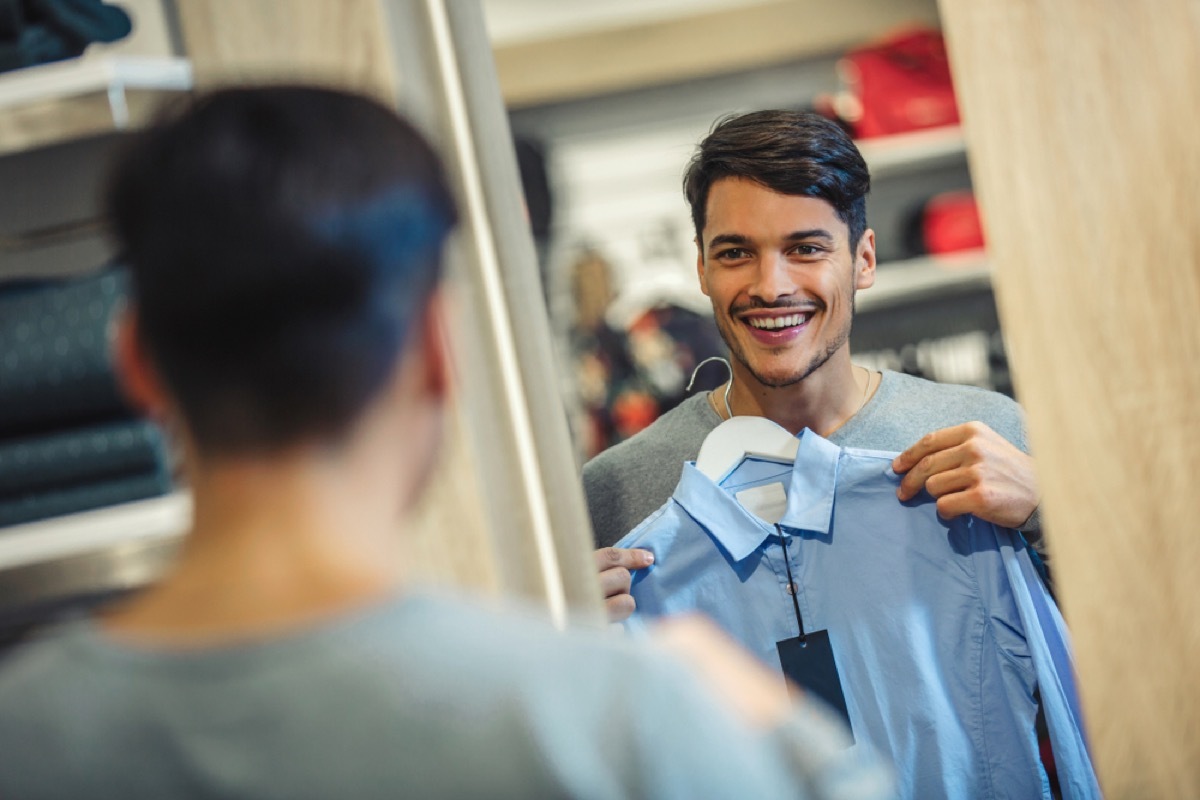 young man looking at shirt in dressing room mirror and smiling