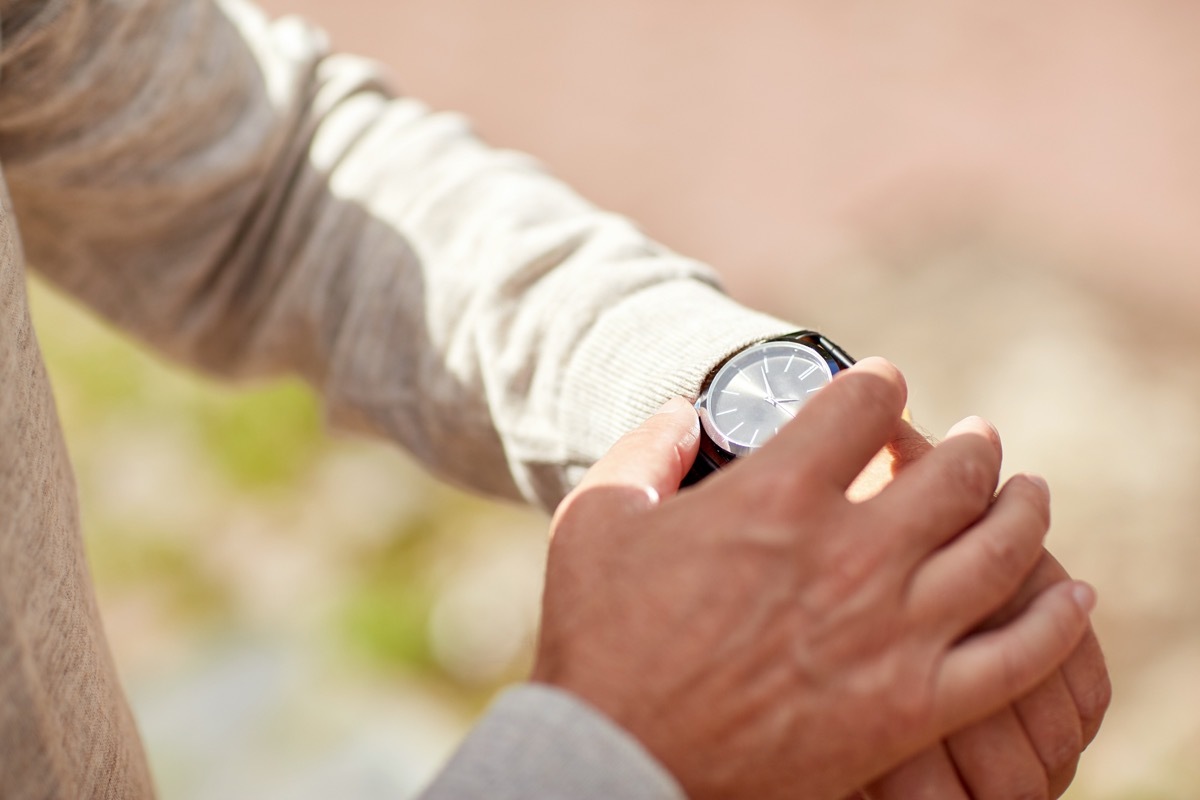 A senior man checking time on wristwatch outdoors.