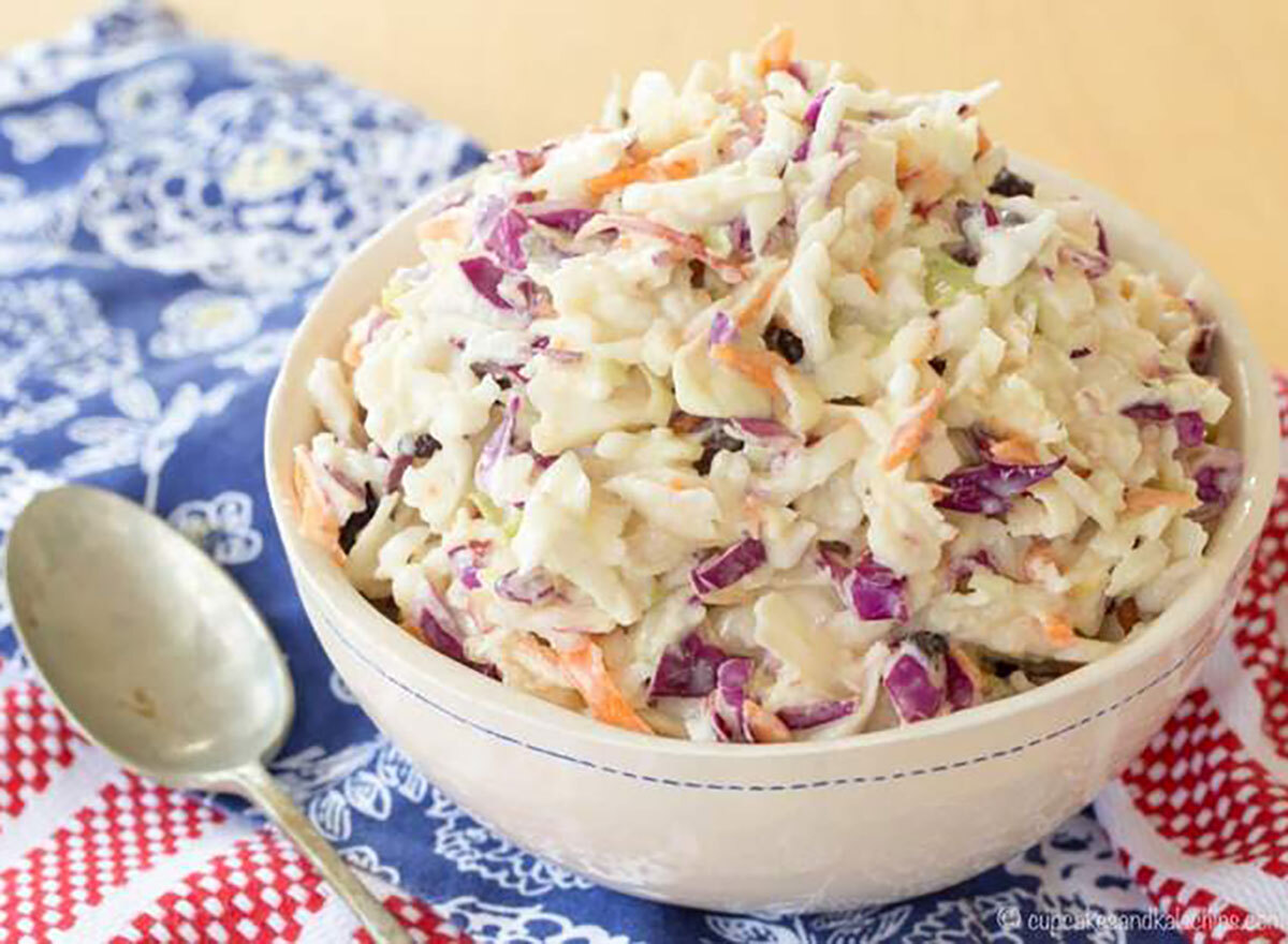 maple dijon apple coleslaw in white bowl with spoon on red white and blue tablecloth