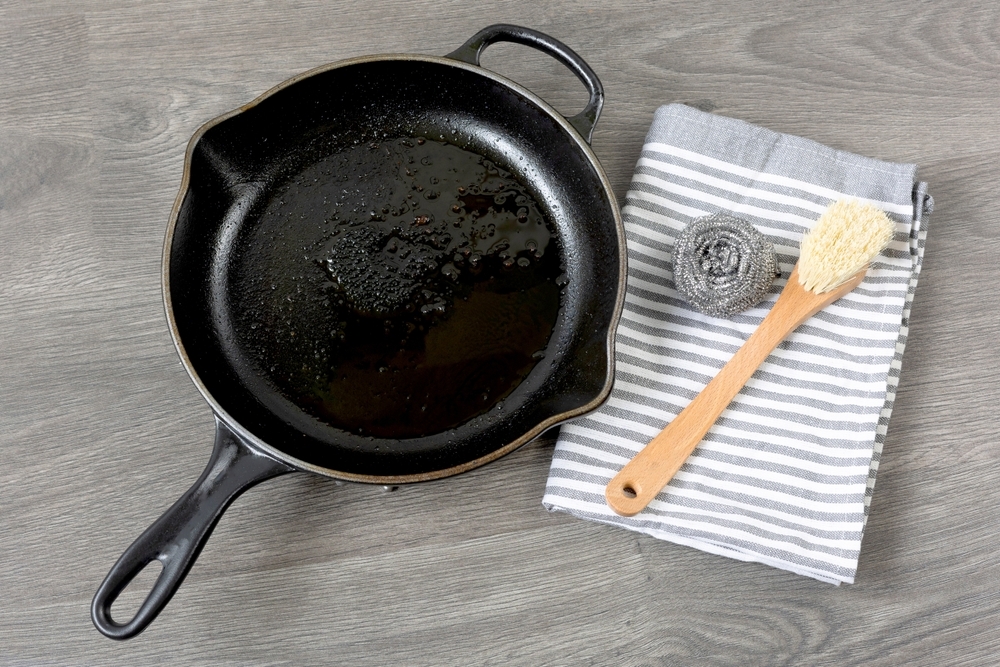 A cast iron skillet sitting next to a brush and iron wool, waiting to be cleaned