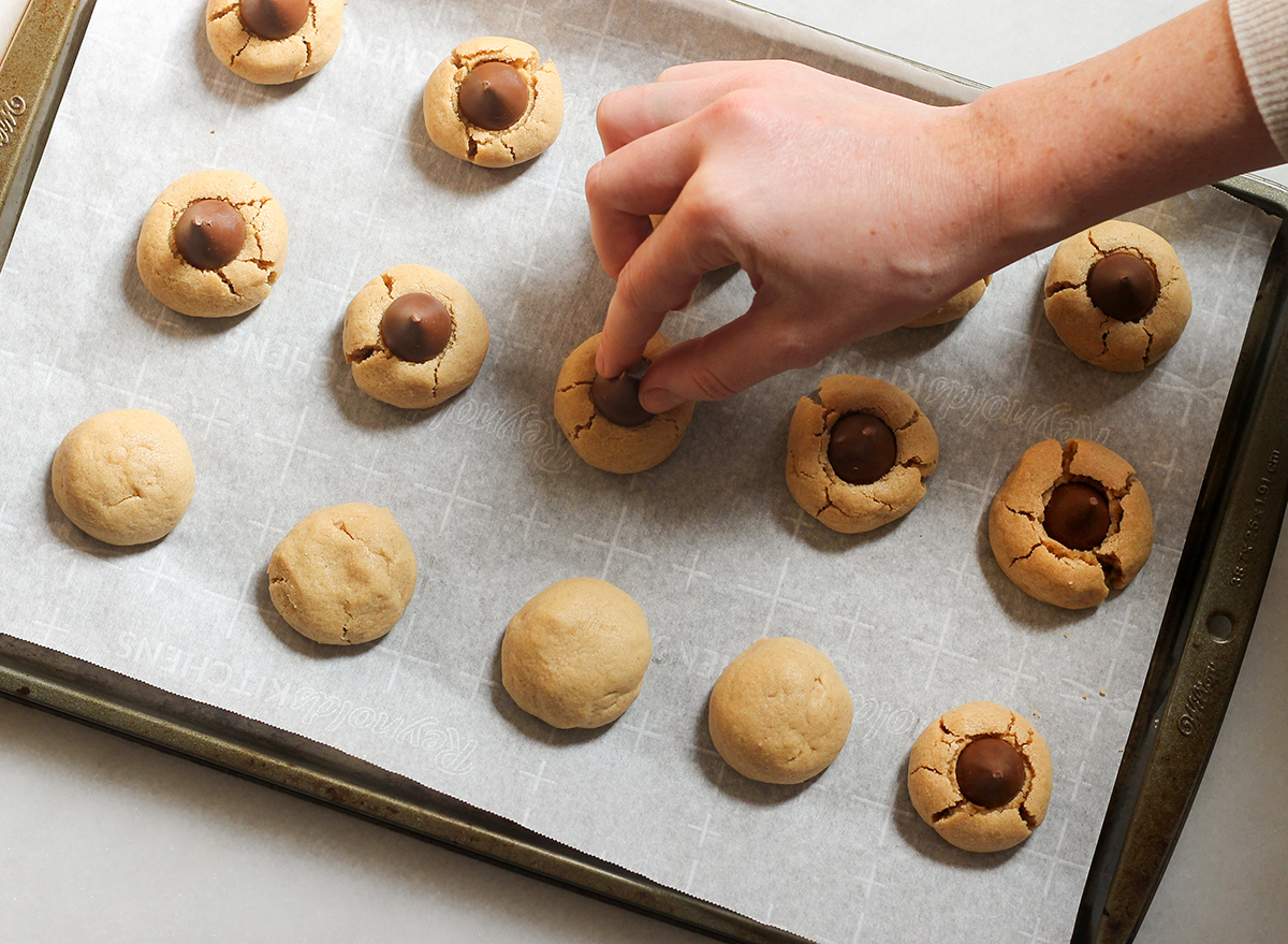 adding chocolates to peanut butter blossoms on a baking sheet