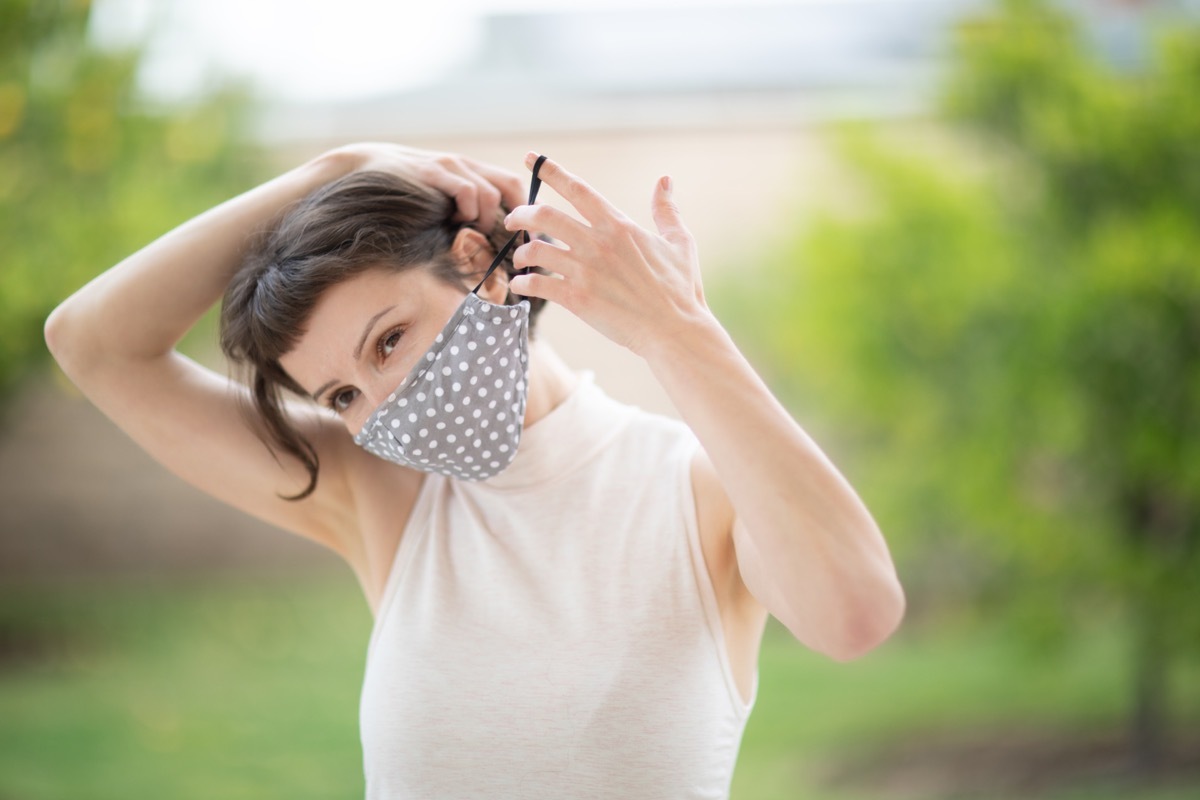young woman with brown hair putting on cloth face mask