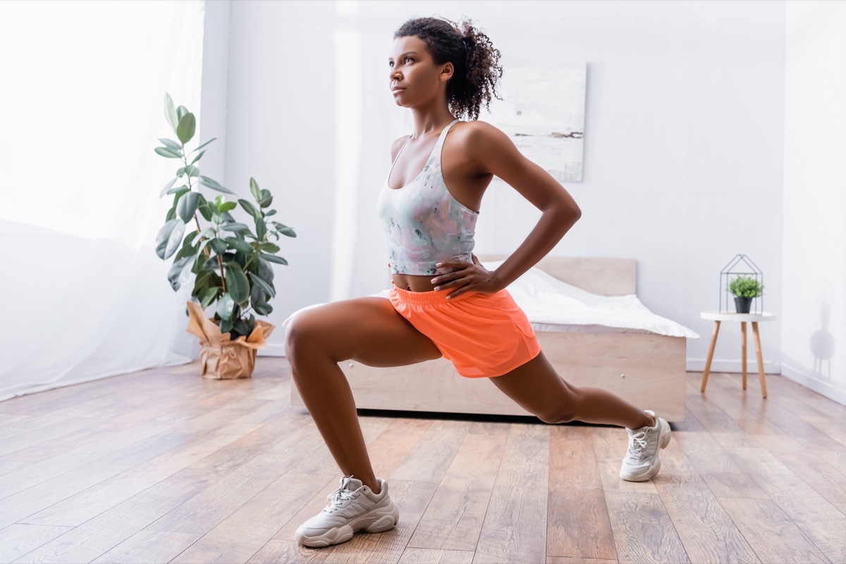 African american woman doing lunges while training in bedroom