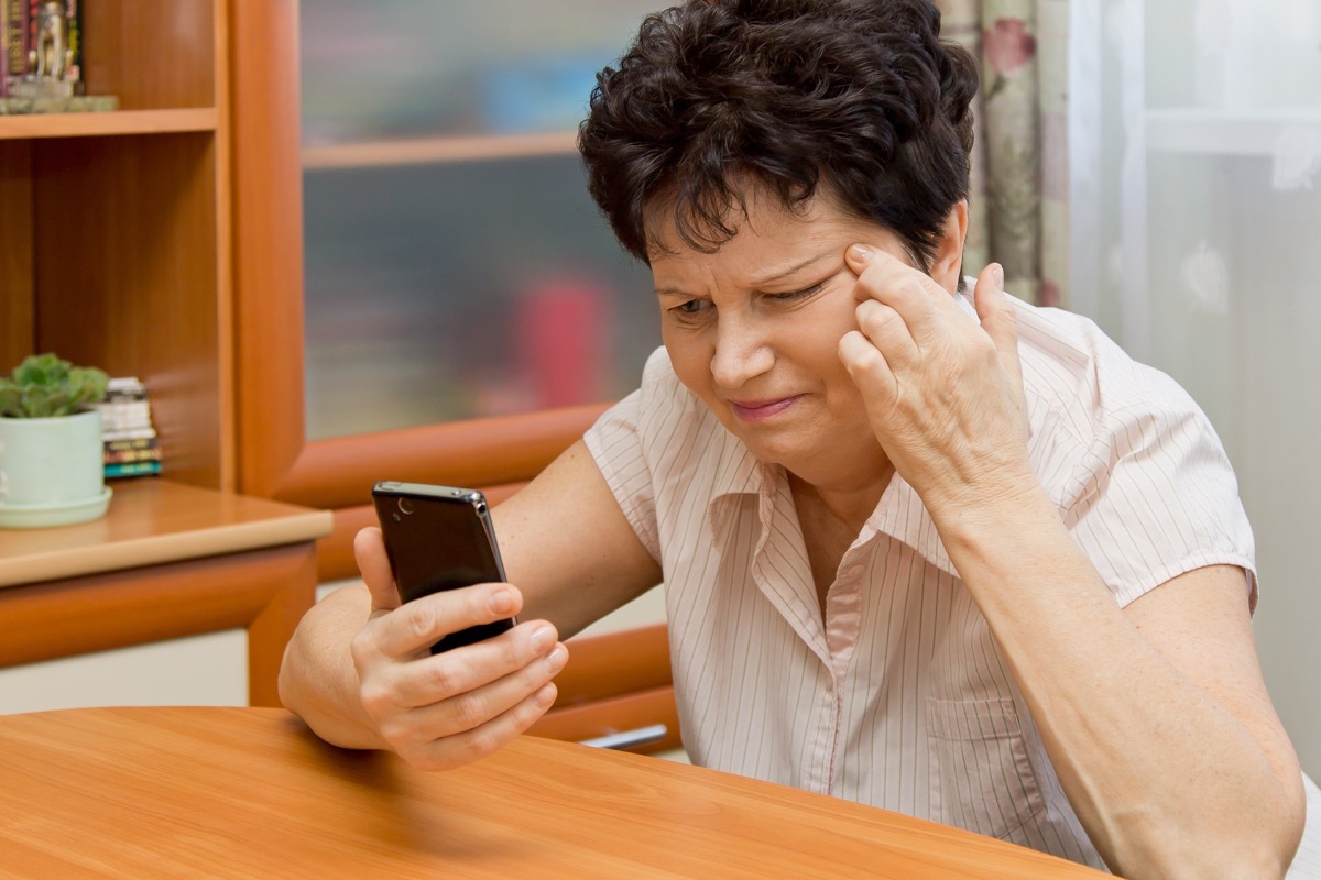 Woman squinting at her phone because she is having trouble seeing