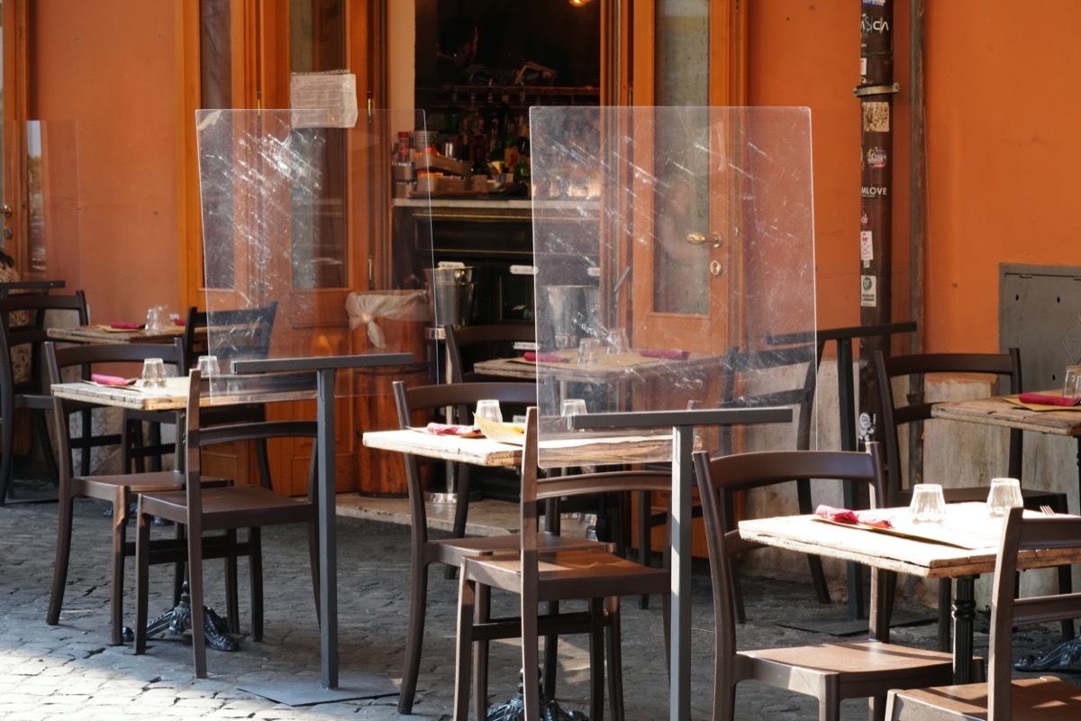 Empty tables outside a restaurant. Plastic, plexiglass screens on for customer separation.