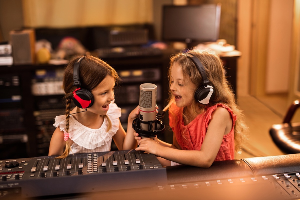 Two small girls having fun in a radio station while talking on a microphone for a podcast