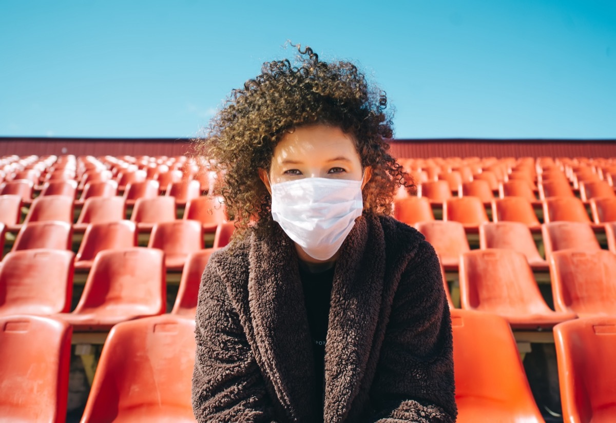 Woman in a surgical mask sitting in an empty stadium.