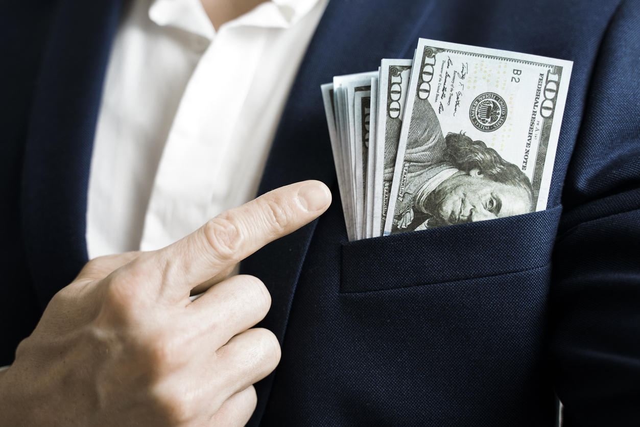 A person pointing to a stack of $100 bills in their breast pocket