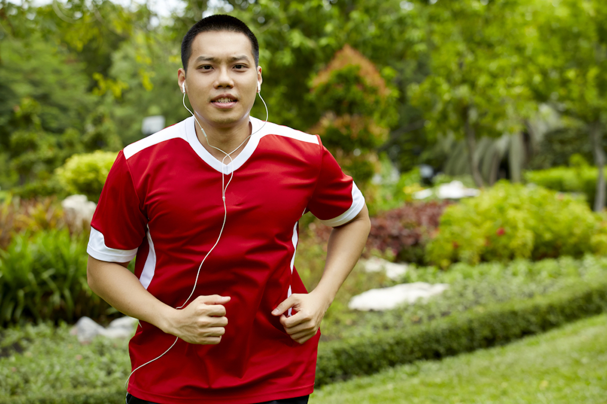 asian man running with headphones in ears, wearing red sports jersey shirt