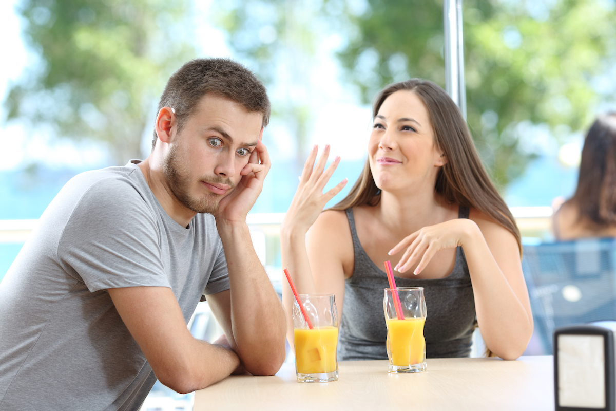 Man looking away and rolling his eyes at a talkative woman while at a restaurant table having orange juice.