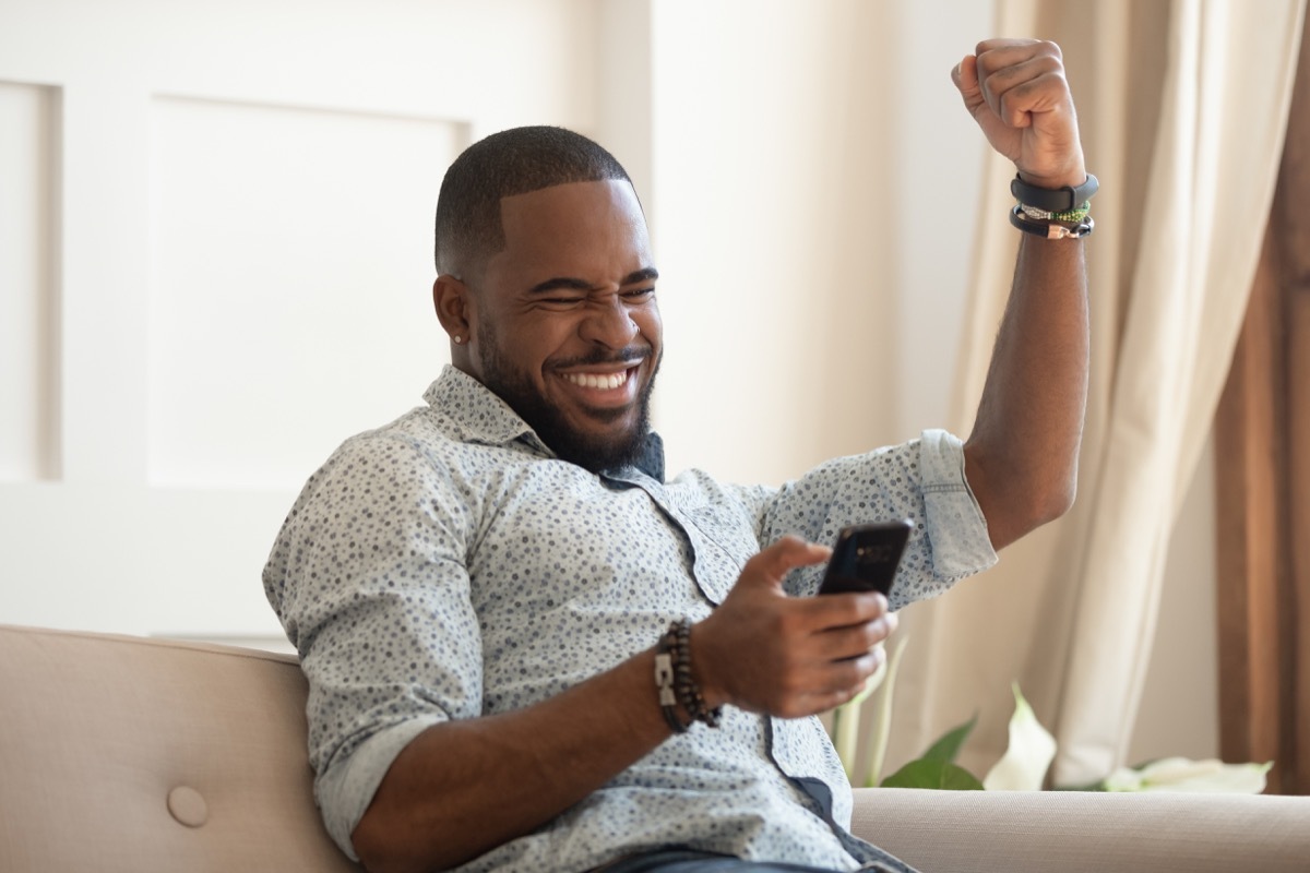 Happy man looking at his phone on the couch cheering
