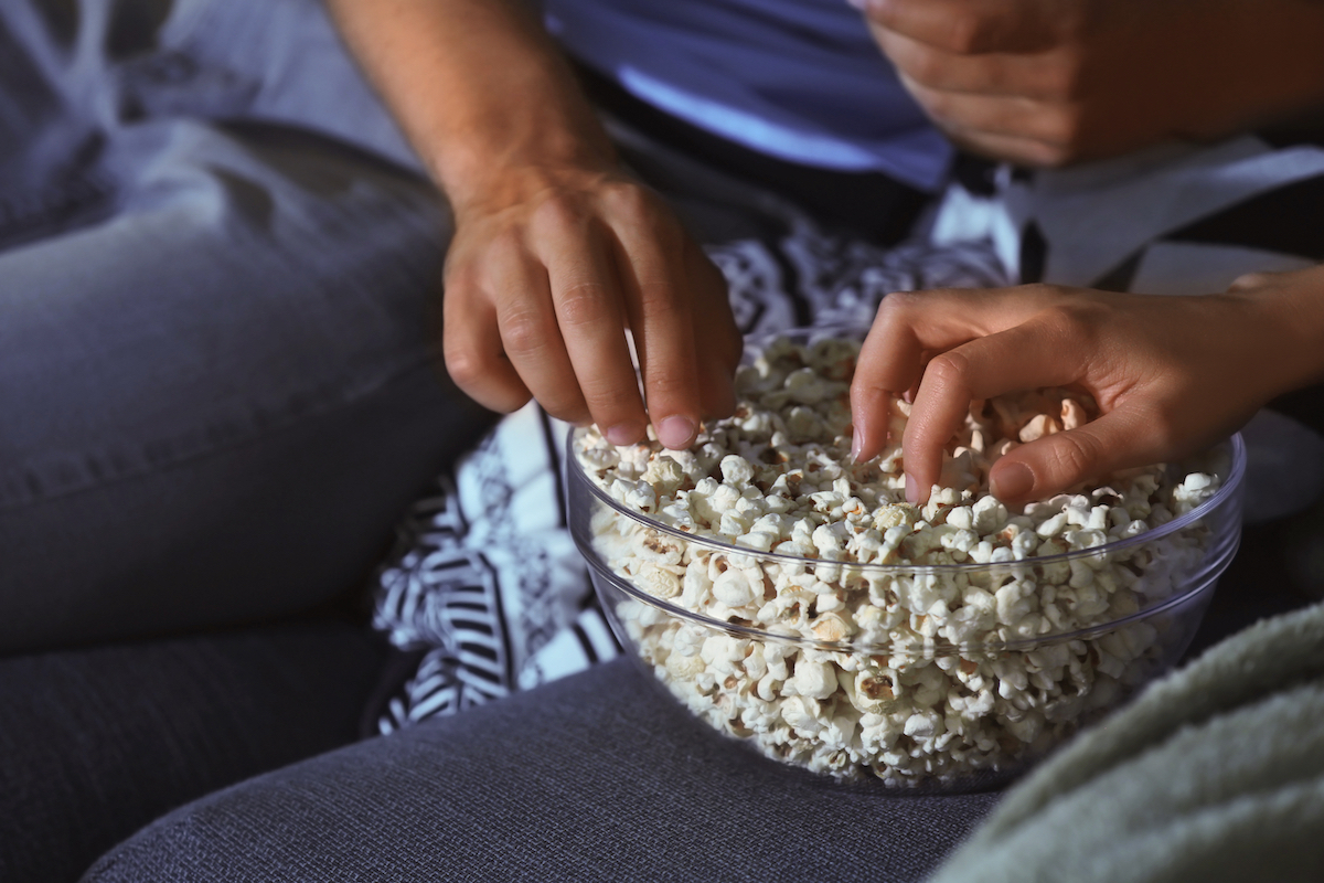 two hands reaching for popcorn in a bowl