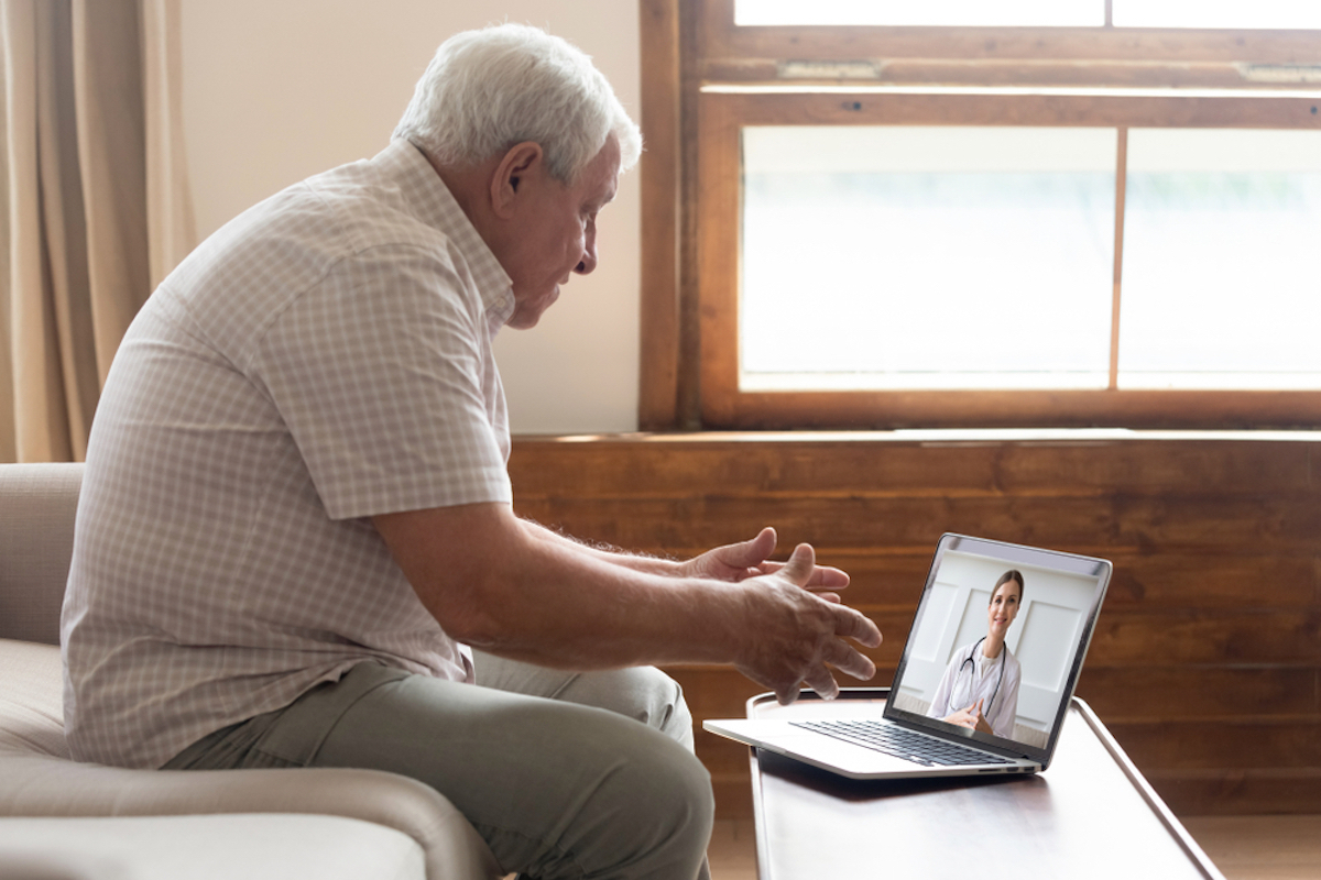 senior man sits on couch talking to doctor via laptop in telehealth appointment