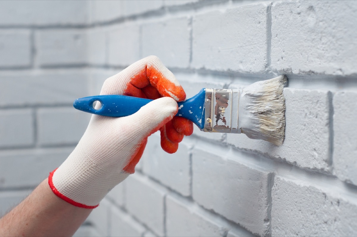 gloved hand painting brick white