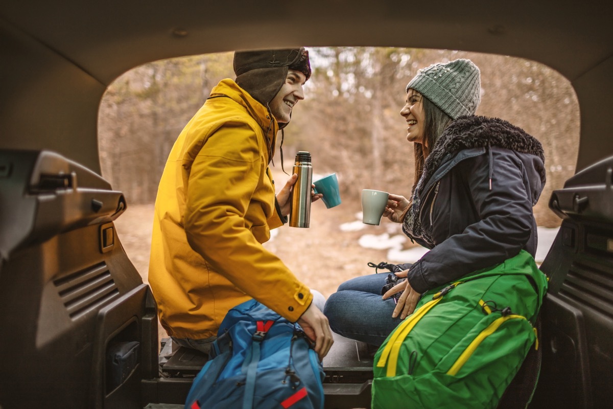 Young couple resting in car trunk after day in nature with hot teaYoung couple resting in car trunk after day in nature with hot tea