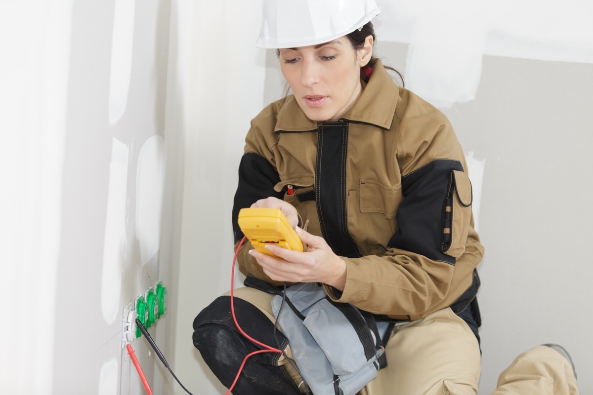 woman wearing hard hat checking an outlet for power