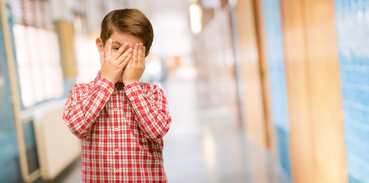 boy covers face in embarrassment in school hallway